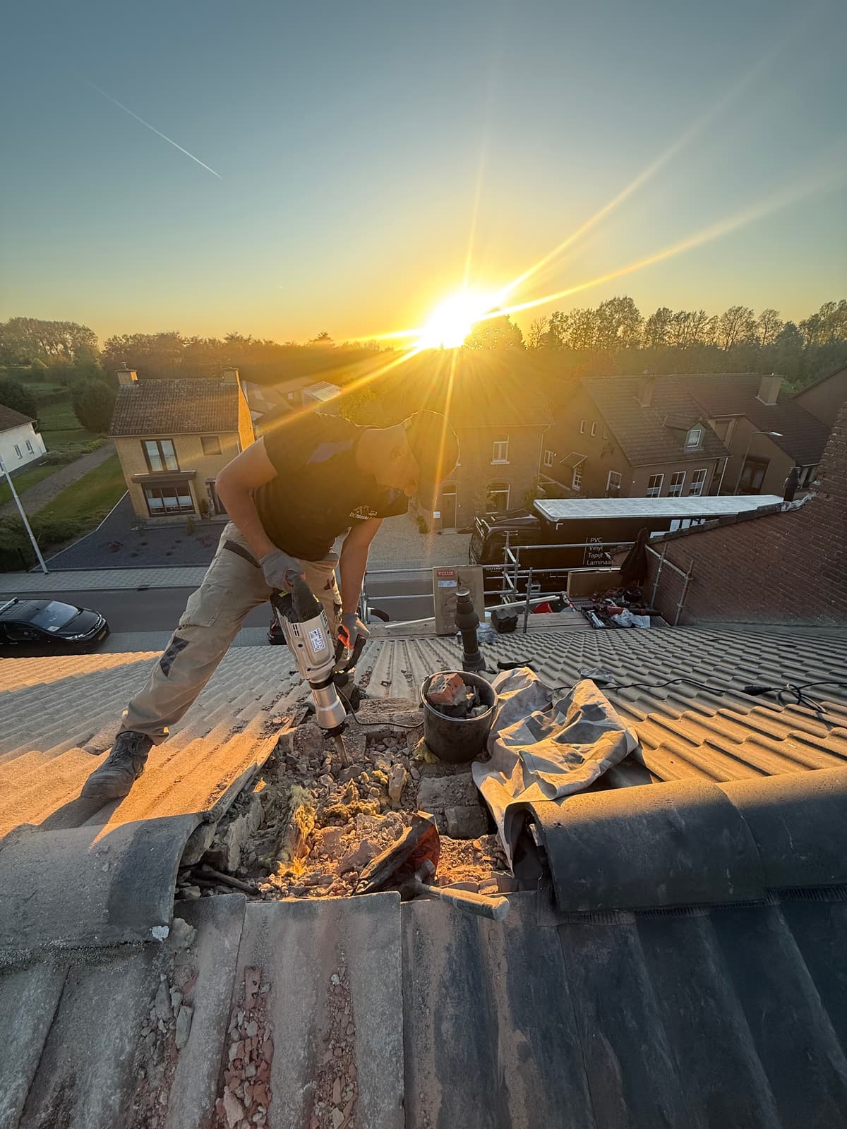 Dakdekker voert reparatiewerkzaamheden uit op een schuin pannendak bij zonsondergang.